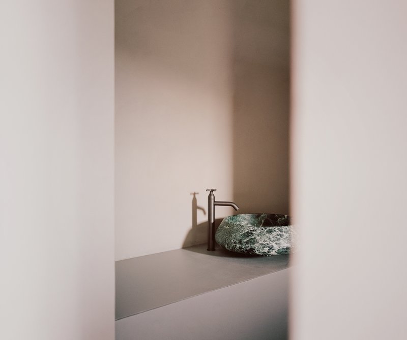 Stone vessel sink with brass faucet on a grey counter framed by pale plastered walls