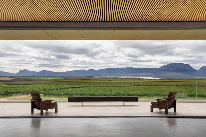 Full-height glass wall framing green fields and distant mountains under an overcast sky