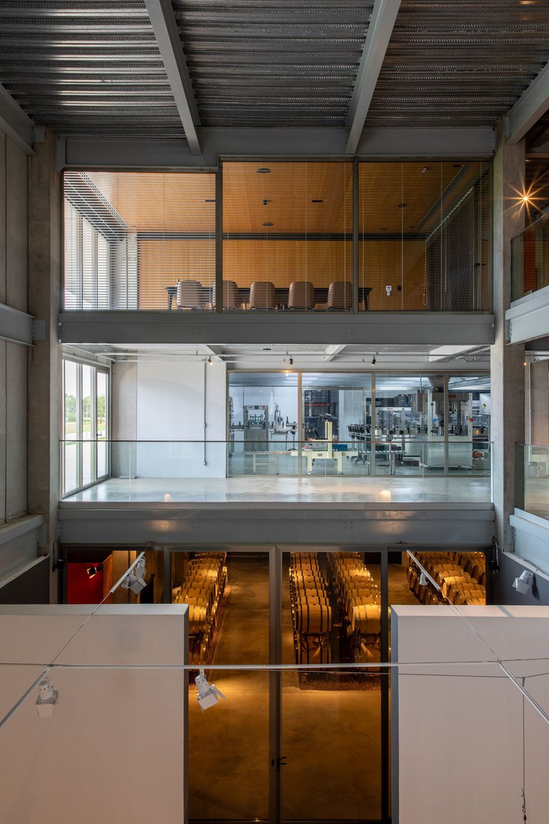Three-story interior atrium showing stacked floors with concrete beams and glass-walled production space below