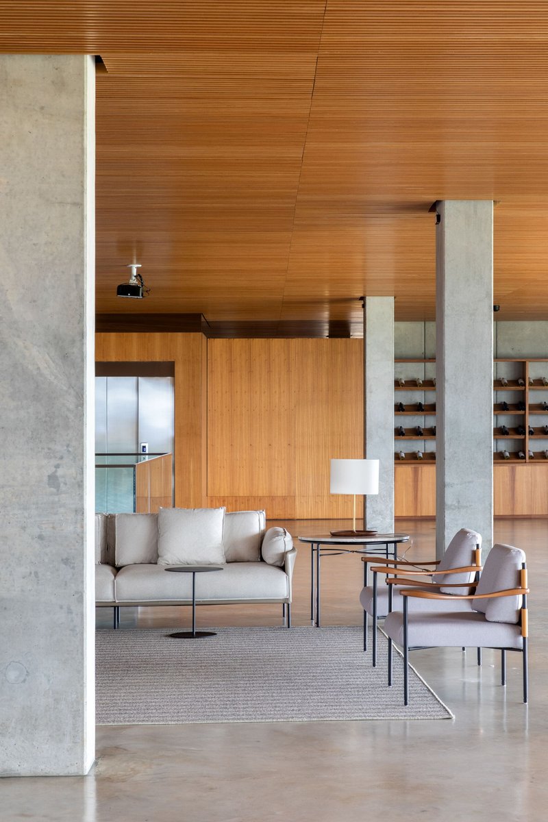 Living area framed by concrete columns with horizontal timber-clad walls and ceiling above polished stone flooring