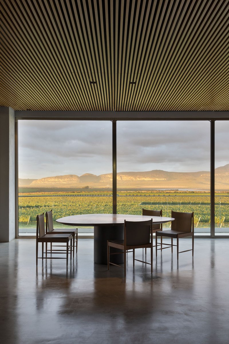 Single dining table beneath radiating timber ceiling slats framing a view of fields and hillsides
