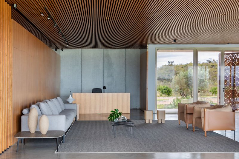 Interior view toward glazed doors framing landscape with concrete walls and timber slat ceiling