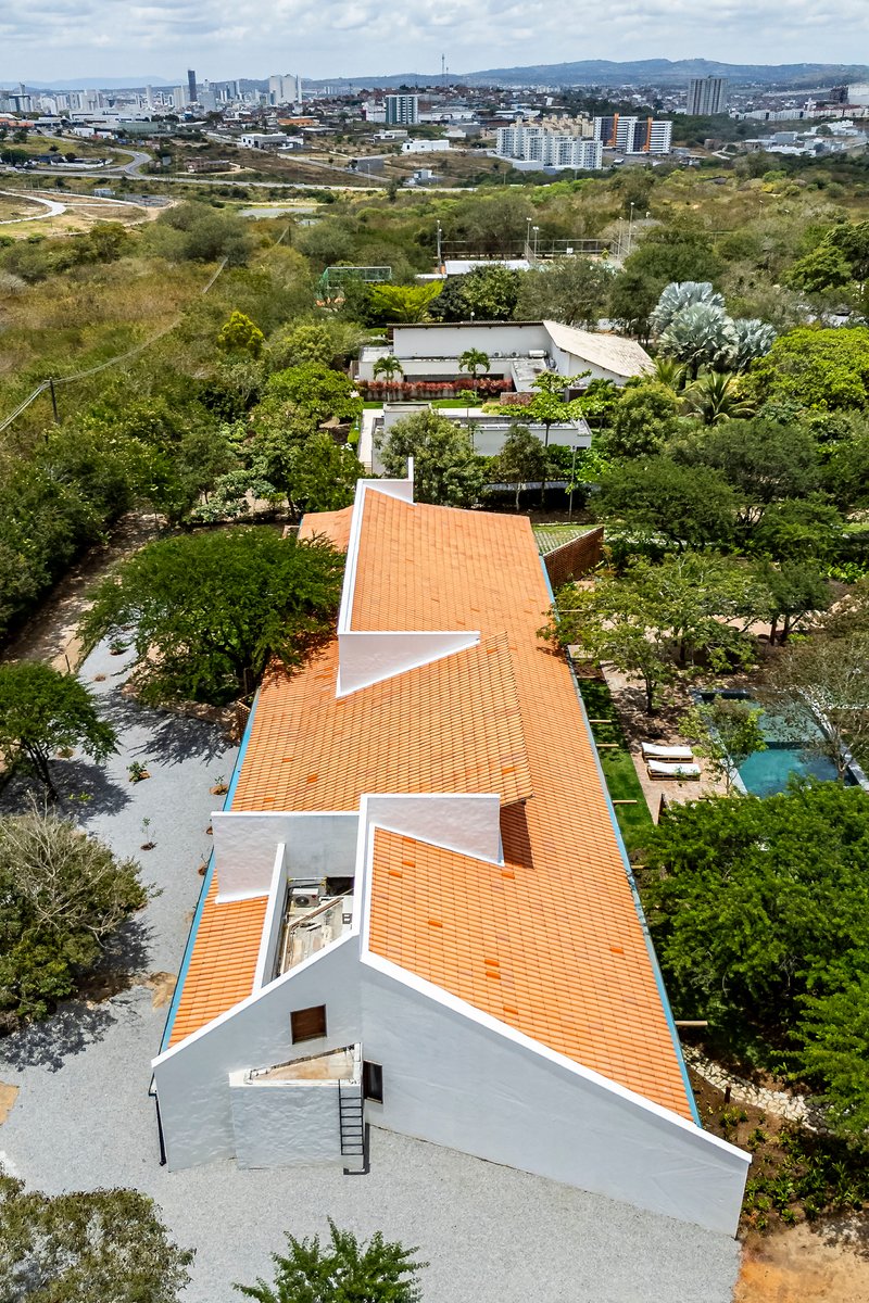 Aerial perspective showing the zigzagging terracotta roof forms between white stucco walls and dense vegetation