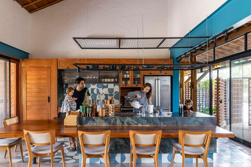 Open kitchen with dark stone island and patterned tile backsplash beneath wire mesh suspended ceiling