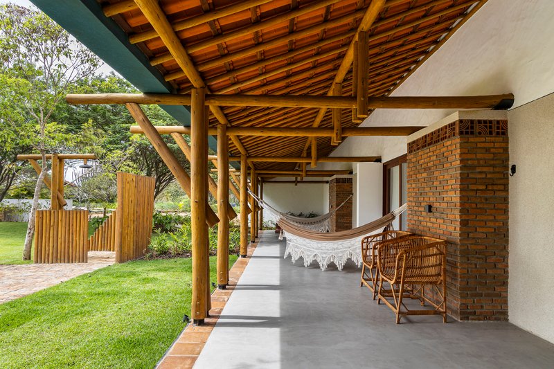 Covered porch with exposed timber rafters, hammock, and brick wall adjacent to lawn and pool