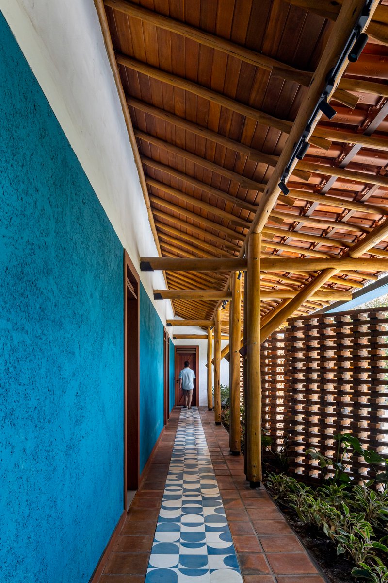 Exterior corridor with blue textured wall, timber roof structure, patterned tile floor, and perforated brick screen