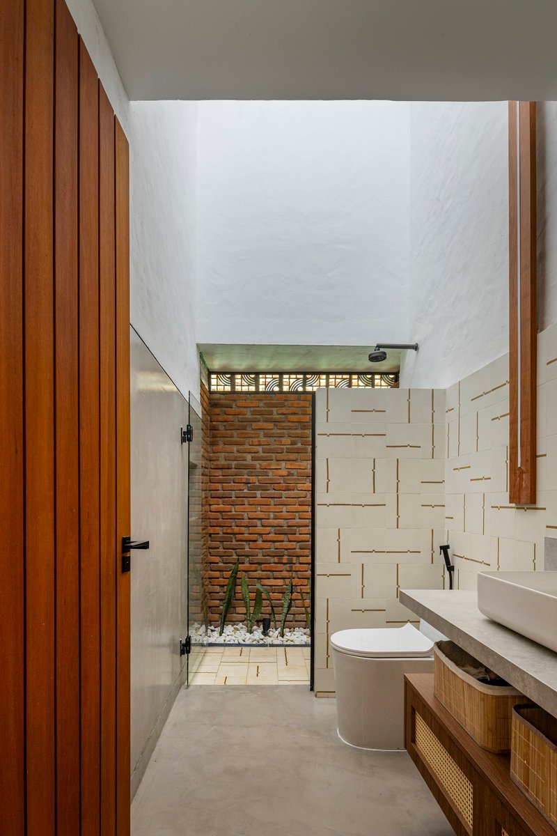 Narrow bathroom with tall ceiling and glass door opening to a brick-walled courtyard with planted gravel bed