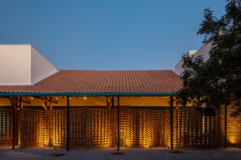 Night view of the perforated brick facade illuminated from within beneath a tile roof at dusk