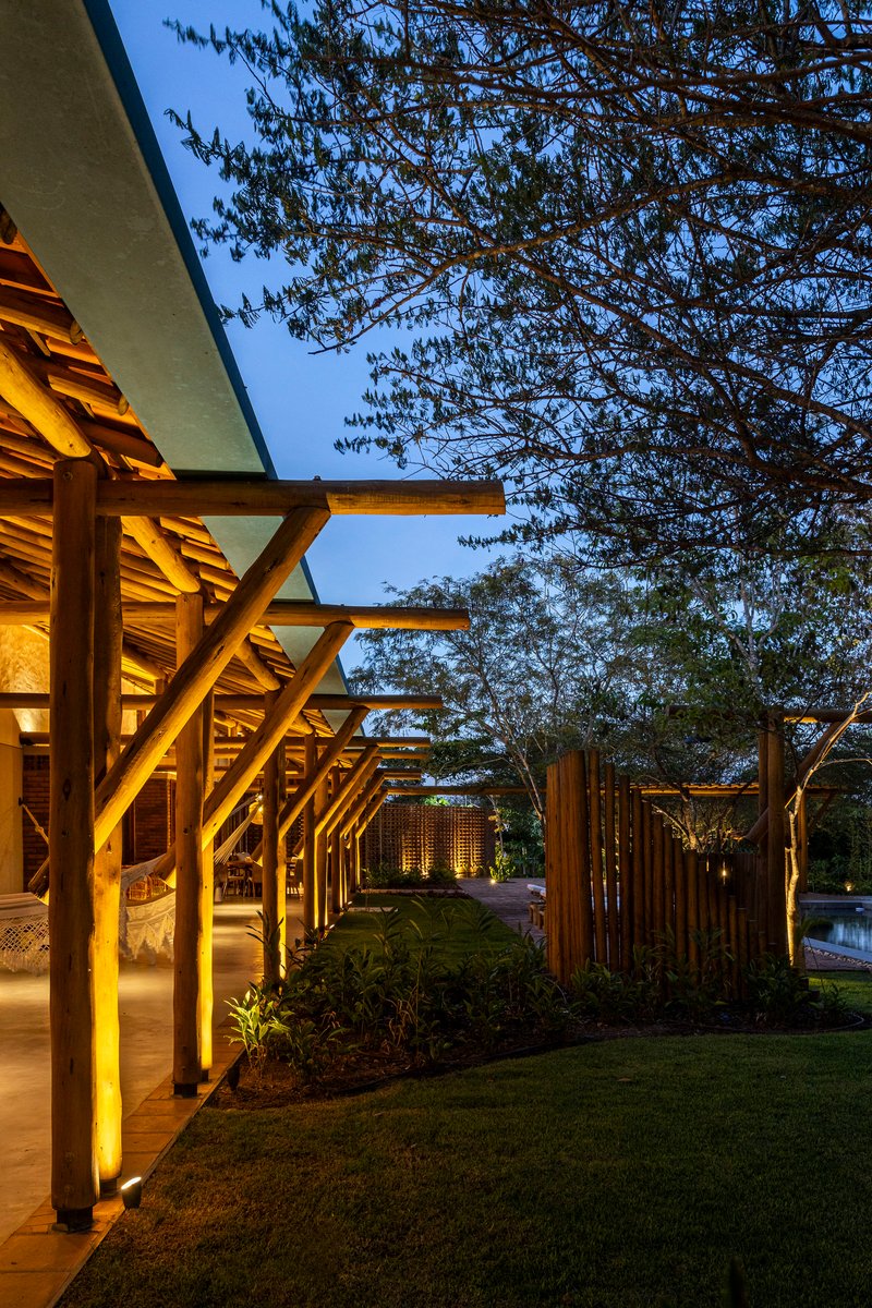 Covered walkway with timber columns and horizontal slats framed by overhanging trees at dusk