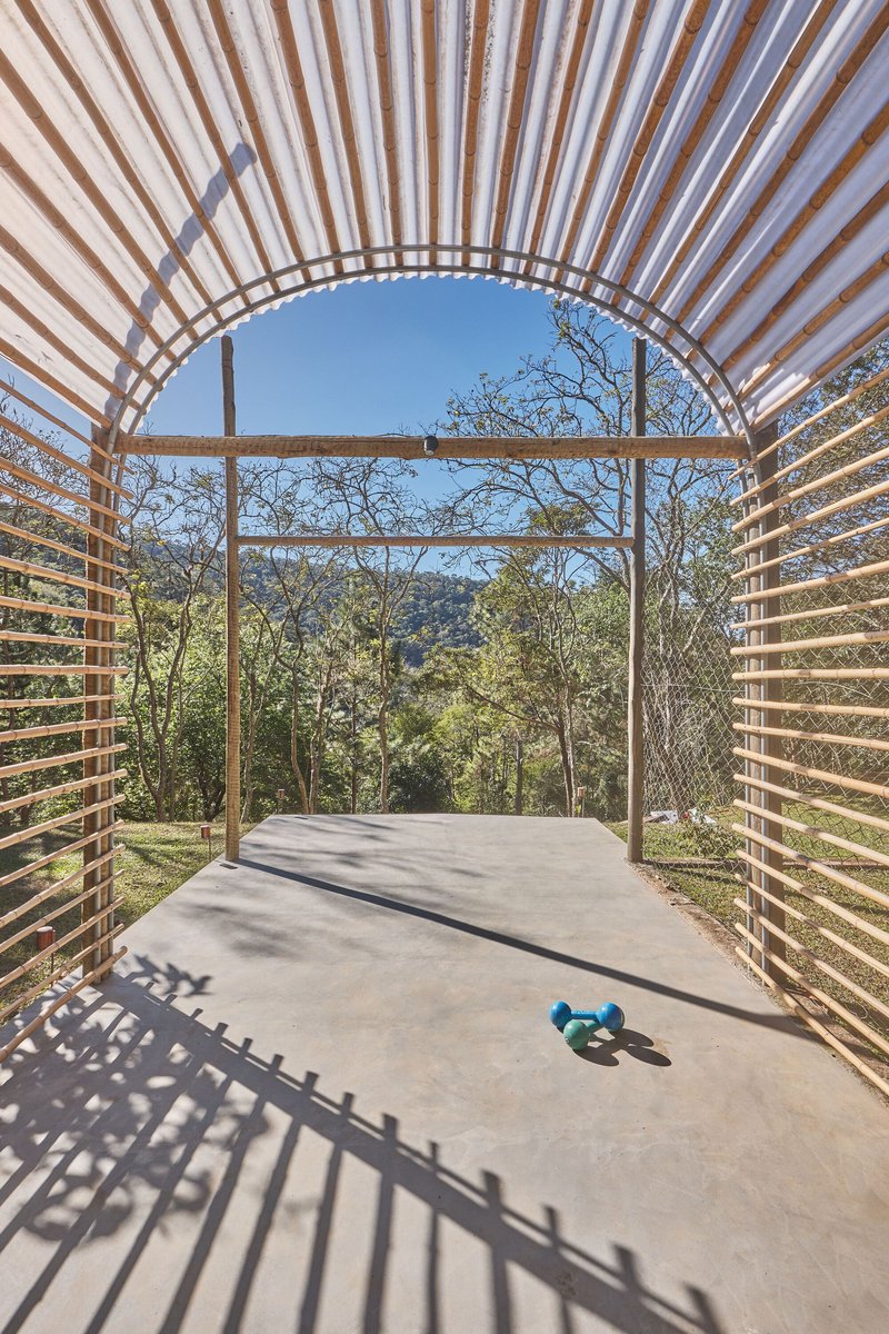 Arched pavilion entrance framing hillside forest view with concrete floor and blue exercise equipment