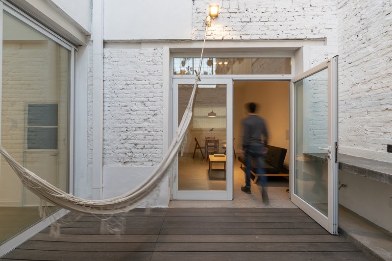 Glazed door opening onto timber deck courtyard with hammock and a blurred walking figure
