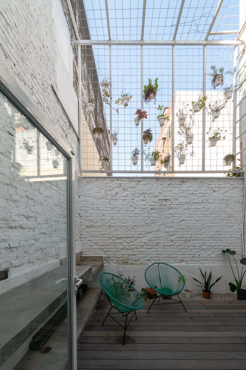 Courtyard with painted brick walls, timber deck and hanging planters suspended beneath wire mesh skylight