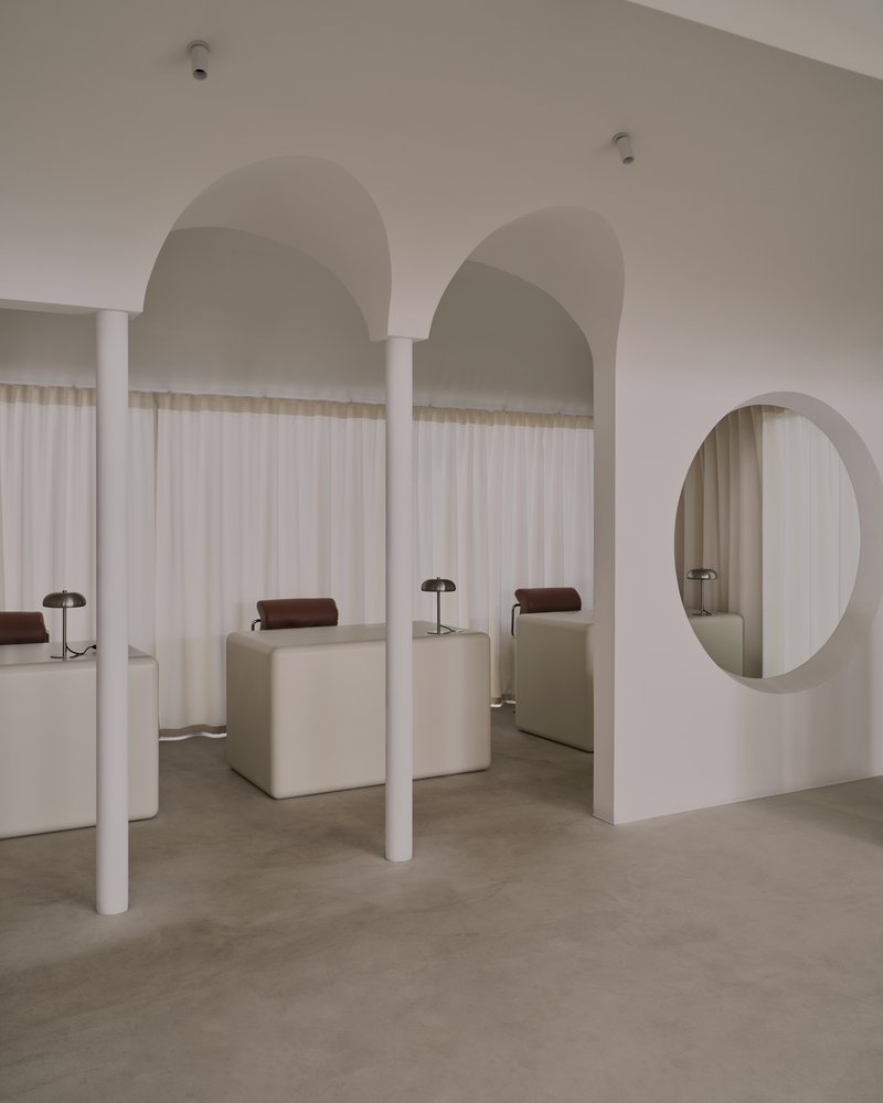 White cylindrical columns framing arched openings and a circular wall mirror under soft overhead lighting