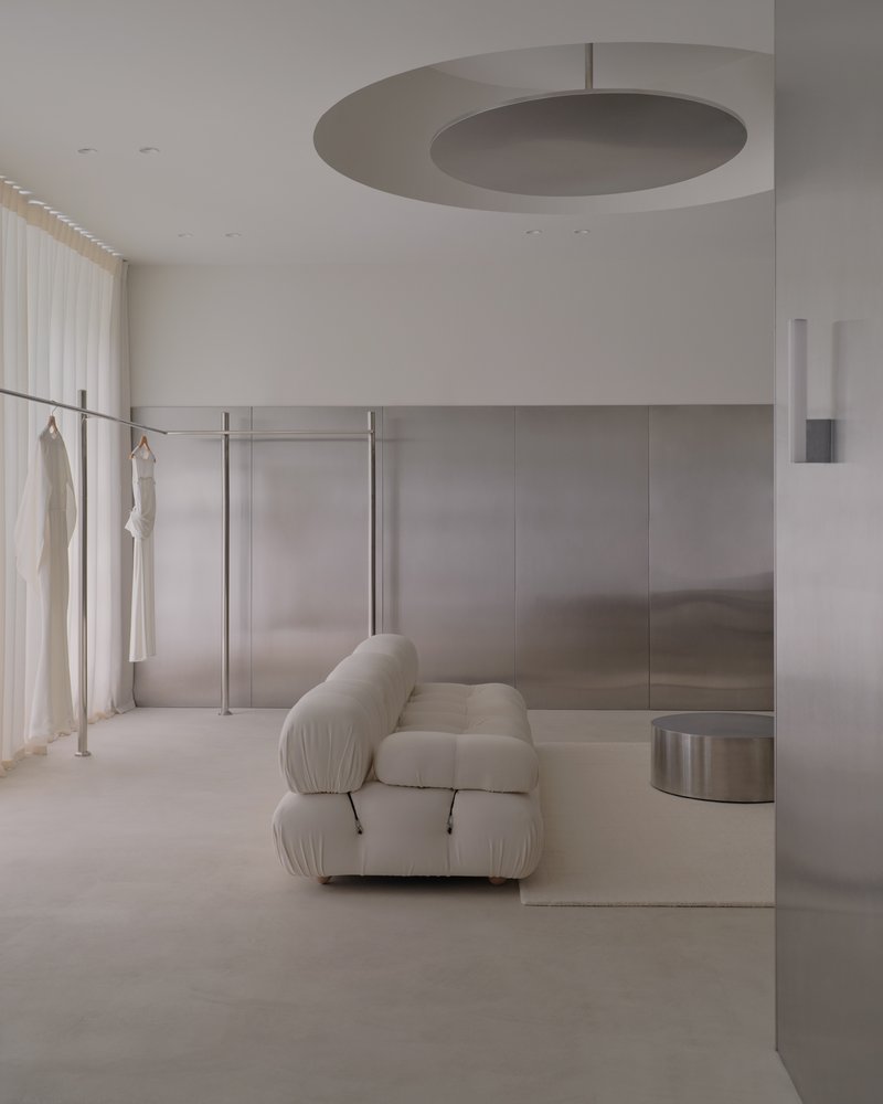 Recessed disc ceiling light above a brushed steel wall panel and freestanding clothing rack