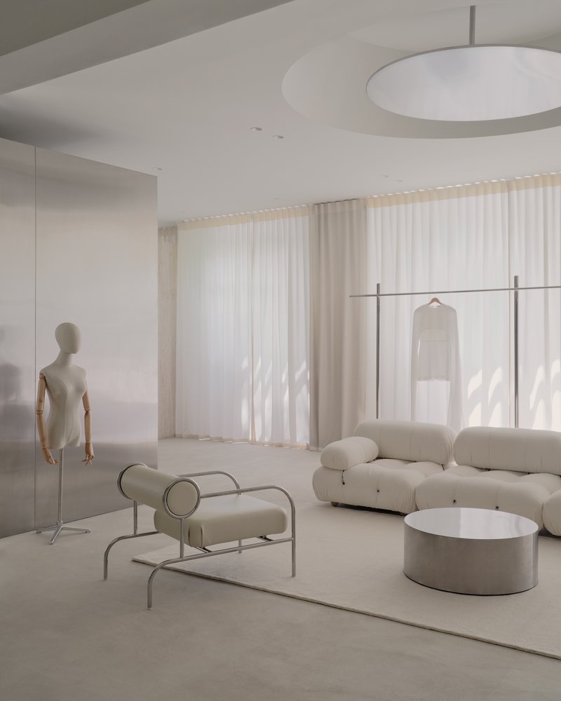 Retail interior with mannequin, tubular seating and sheer curtains filtering natural light from windows