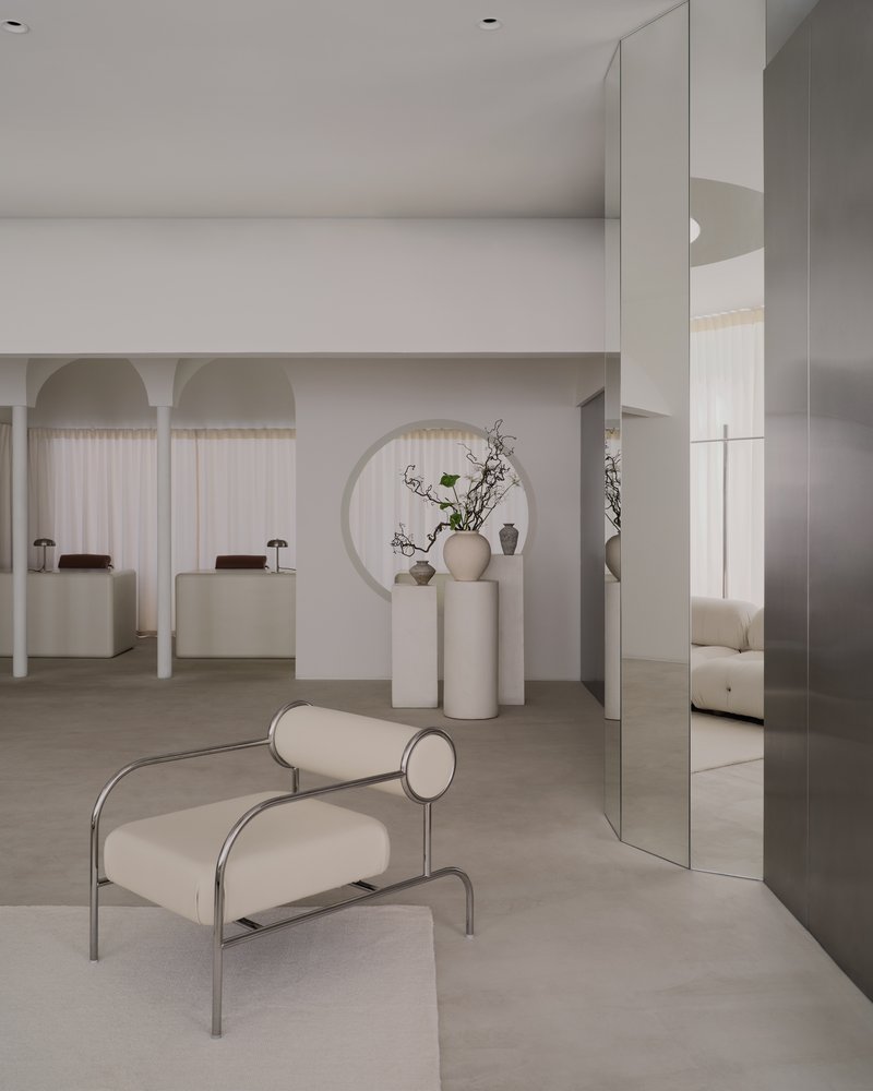 Reception area with tubular steel chair, mirrored panels, and cylindrical pedestals displaying ceramic vessels and branches