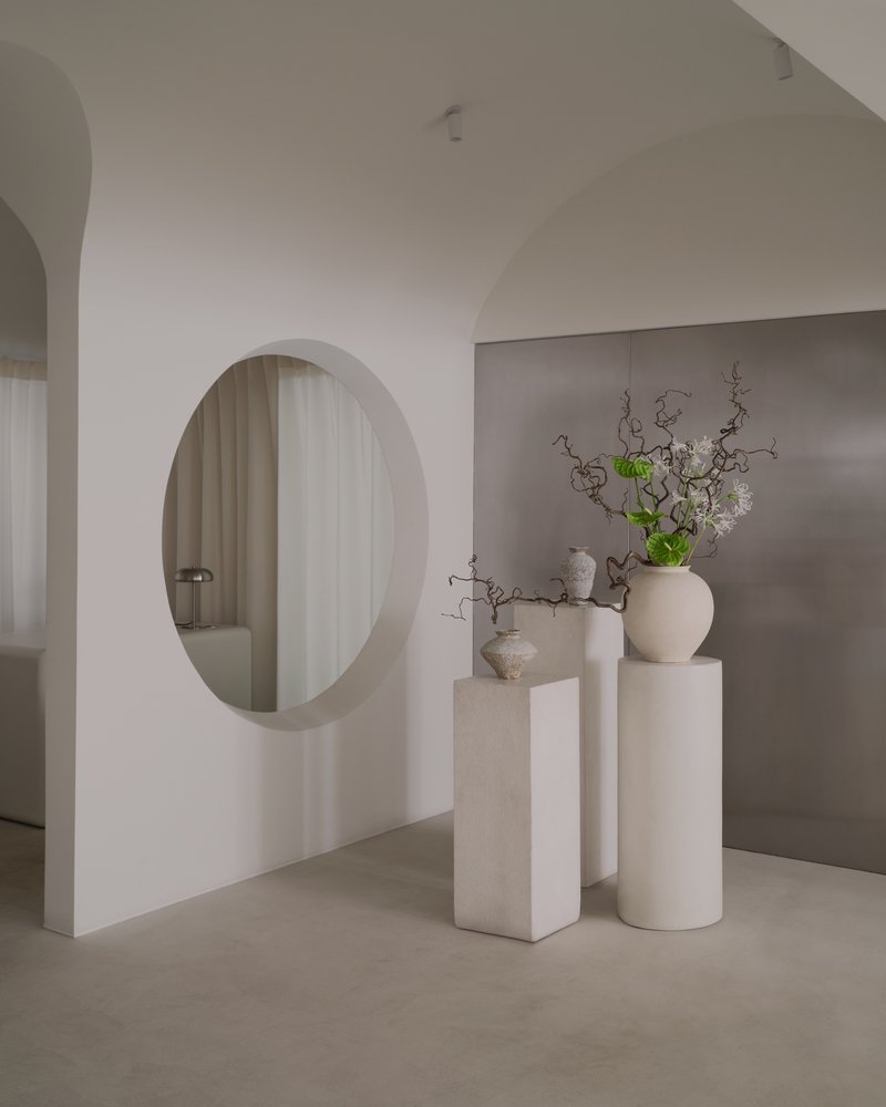 Circular aperture in white wall framing view of sheer curtains with ceramic vases on pedestals in foreground
