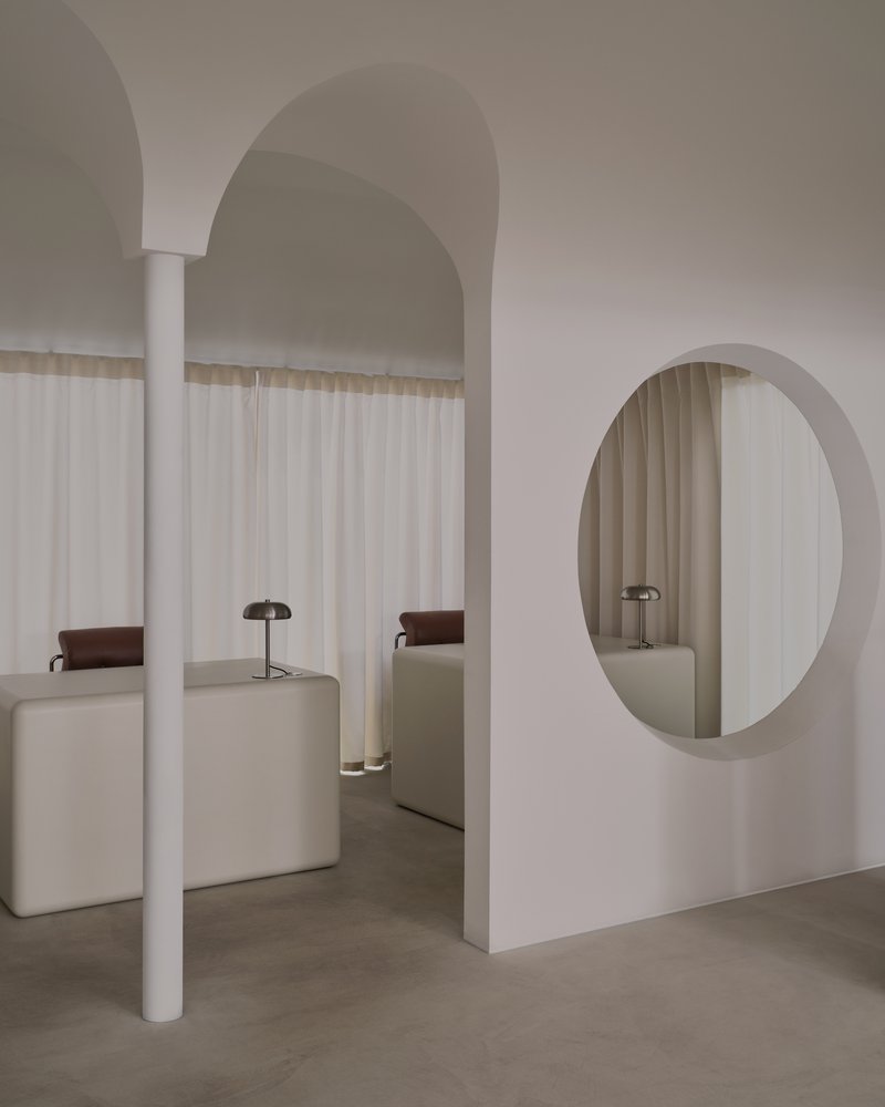 White cylindrical column supporting arched ceiling vault with oval mirror and arched alcoves in background
