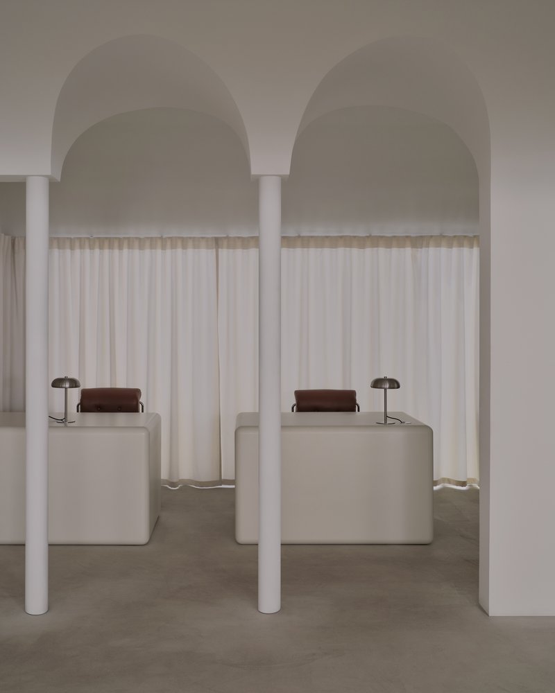 Symmetrical pair of arched alcoves with white columns, sheer curtains, and upholstered seating blocks with table lamps