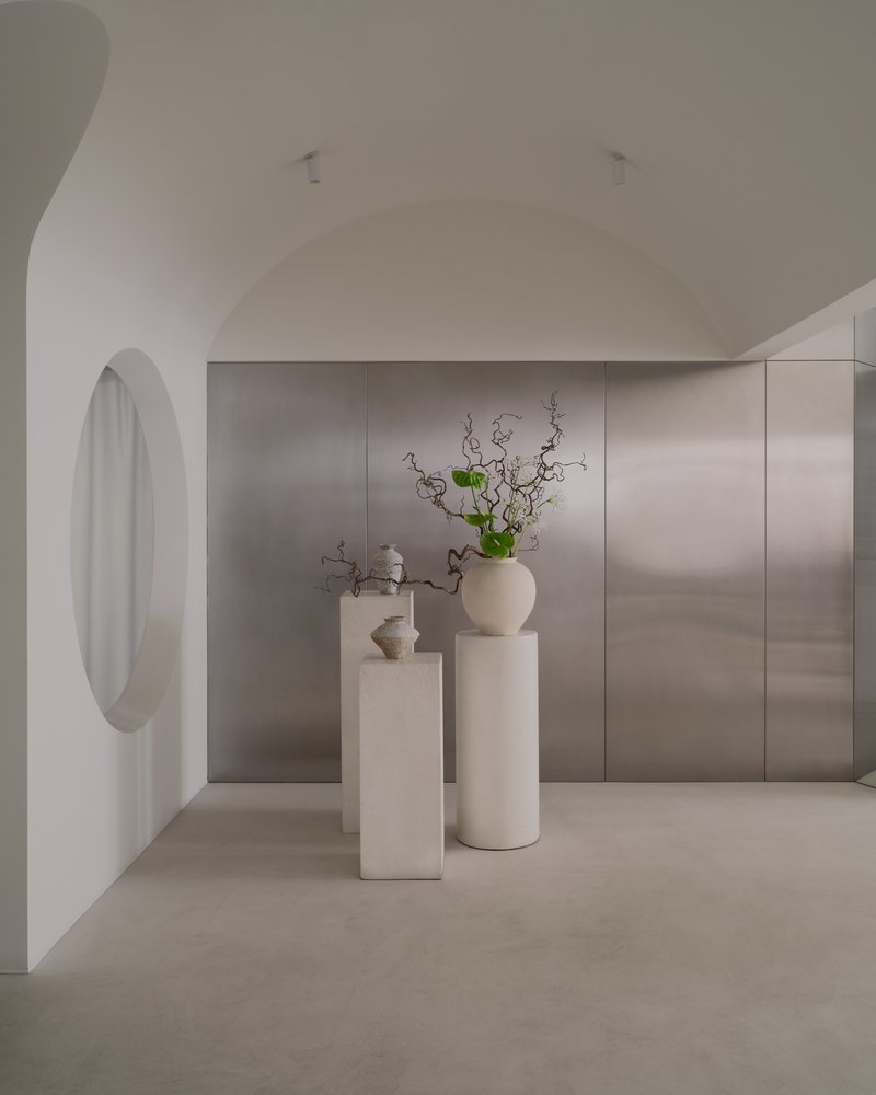 Arched hallway with circular window opening onto stone-paneled wall and ceramic pedestals with green branches