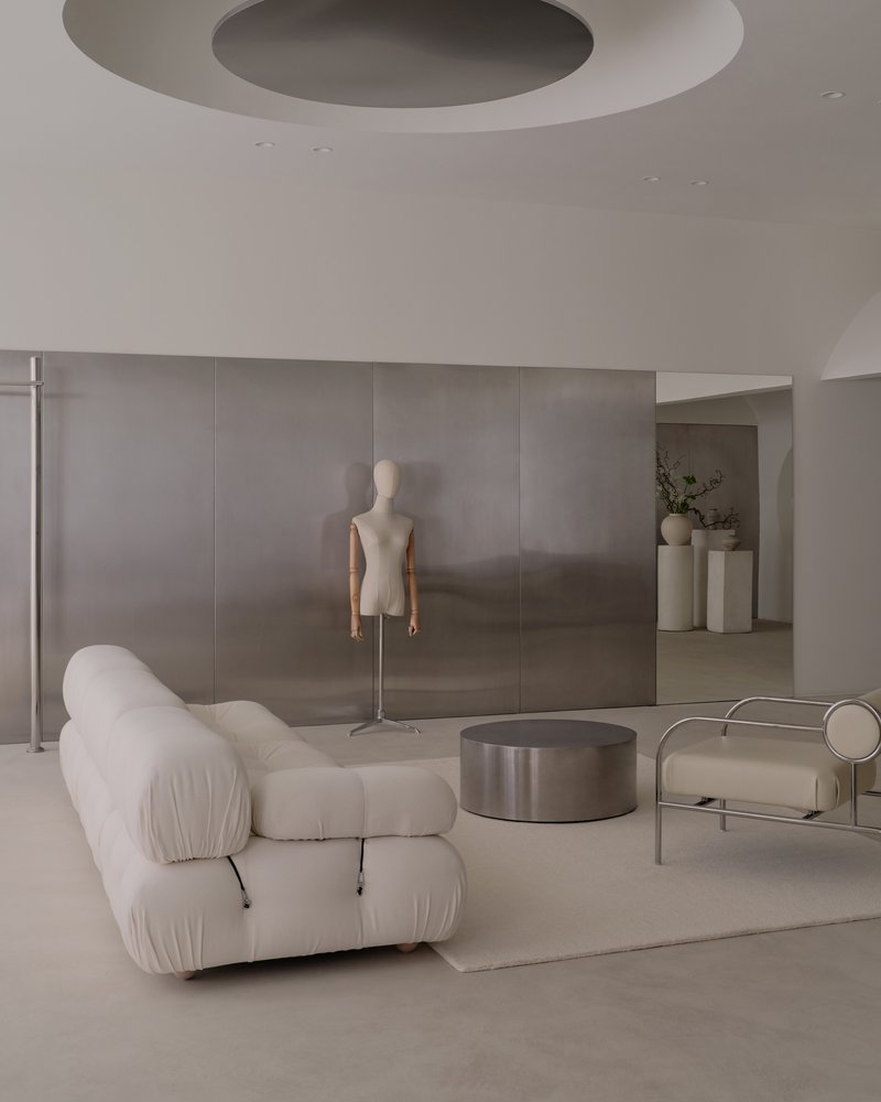 Retail interior with circular ceiling recess, dress form mannequin, and brushed metal coffee table