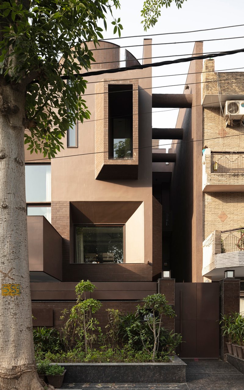 Street facade with geometric bronze-framed windows and planted bed framed by a street tree