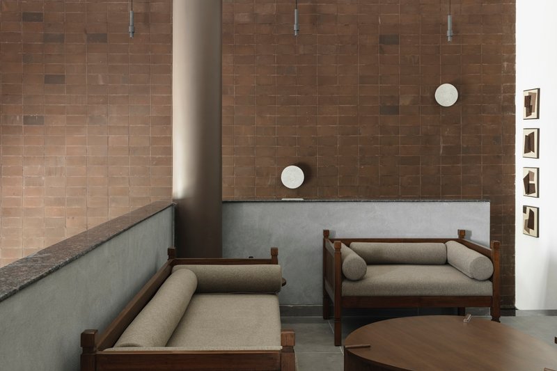 Seating area with brown tile wall and cylindrical column rising through polished concrete floor
