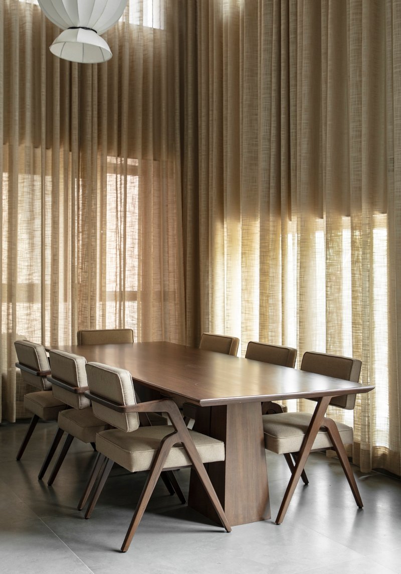 Dining area with timber table and chairs beneath layered linen curtains filtering soft daylight