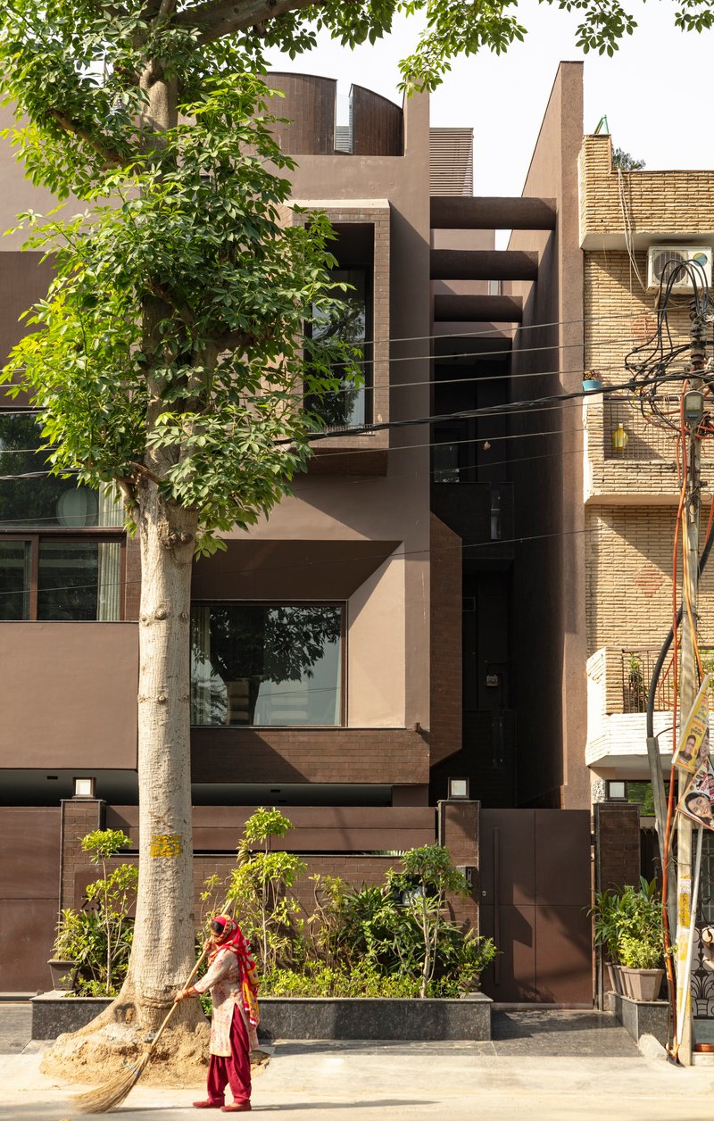 Street facade with layered volumes in plaster and brick framed by trees and a passing pedestrian