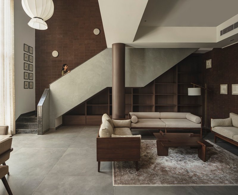 Double-height living space with pale staircase, cylindrical column, timber seating, and pendant light overhead