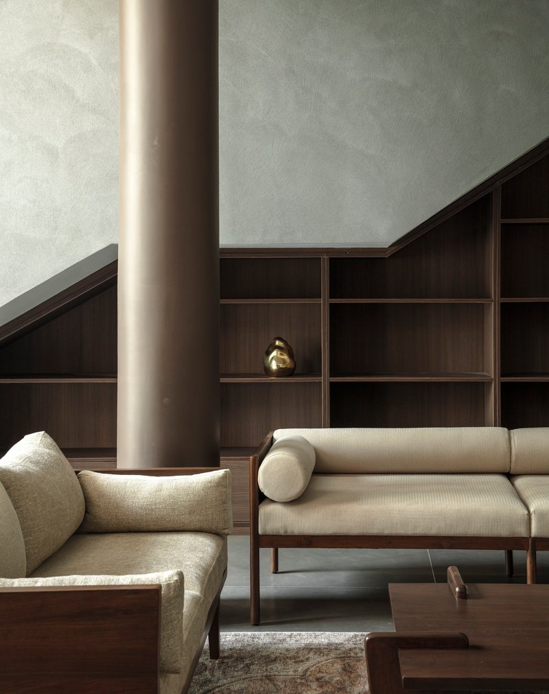 Close-up of cylindrical column beside timber-framed sofa and gridded shelving with small brass object