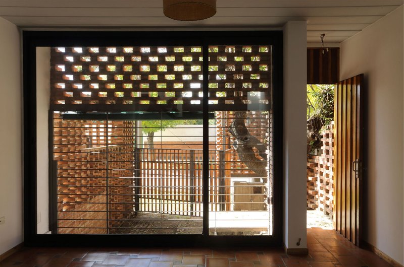 Interior view through glazed doors framing the perforated brick courtyard and timber slats beyond