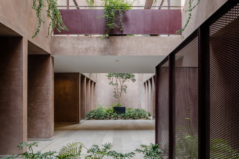 Interior courtyard with perforated metal screens, concrete columns, and cascading vines from the upper balcony