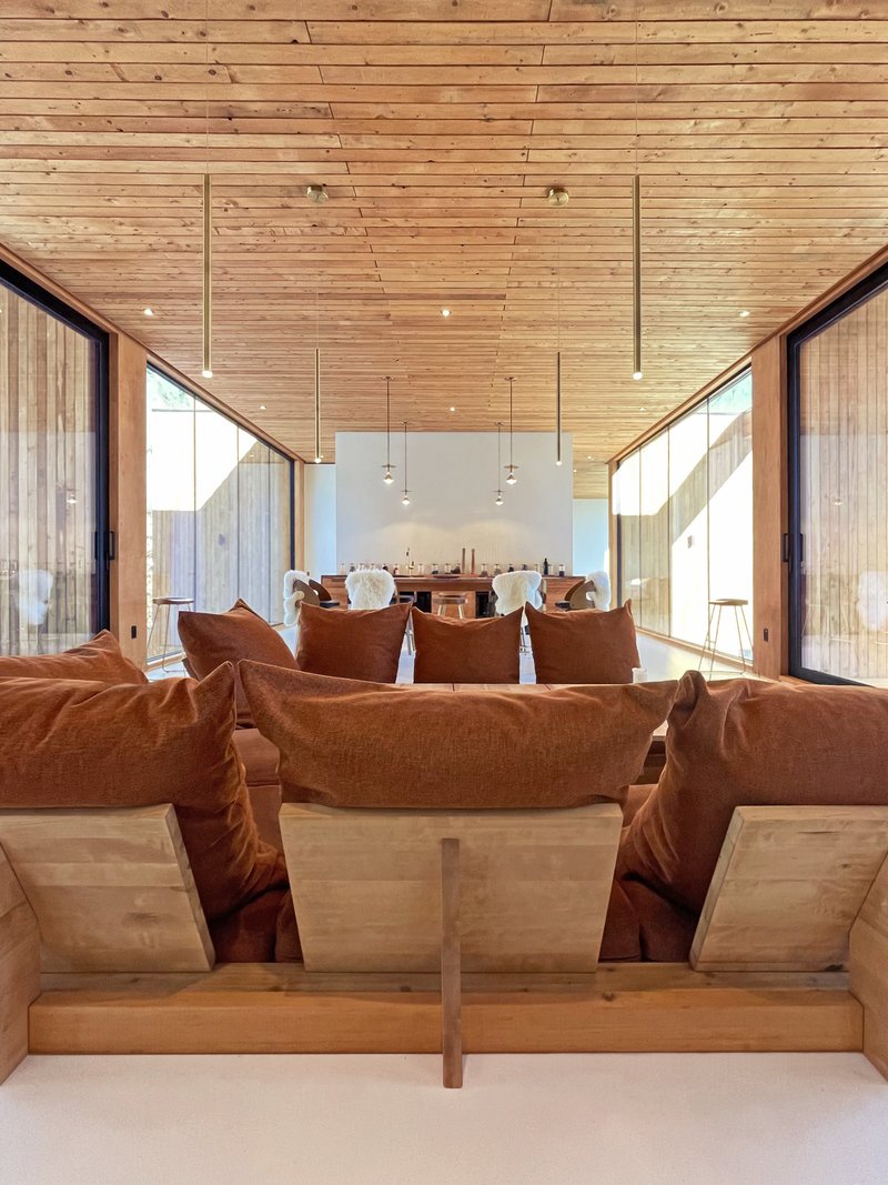 Sunken seating area with diagonal wood planking ceiling and corner windows framing wooded landscape