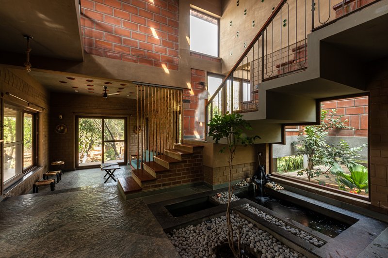 Double-height entry hall with timber and steel staircase beside an interior courtyard planted with a young tree