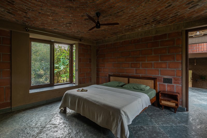 Bedroom with exposed red brick walls and vaulted ceiling with a window overlooking green foliage