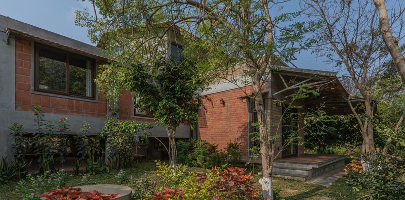 Courtyard view of the brick volumes with overhang and planted garden beds beneath mature trees