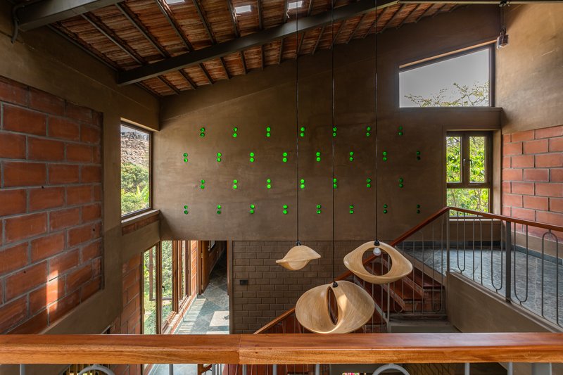 Double-height interior with timber ceiling beams, clay brick walls, pendant lights, and metal railings around a central void