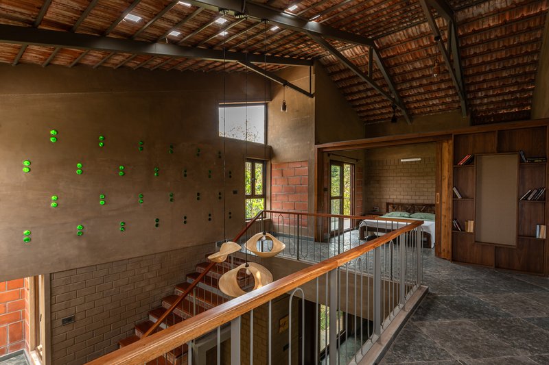 Interior mezzanine with diagonal timber handrail, clay brick walls with green lighting fixtures, and gabled timber ceiling