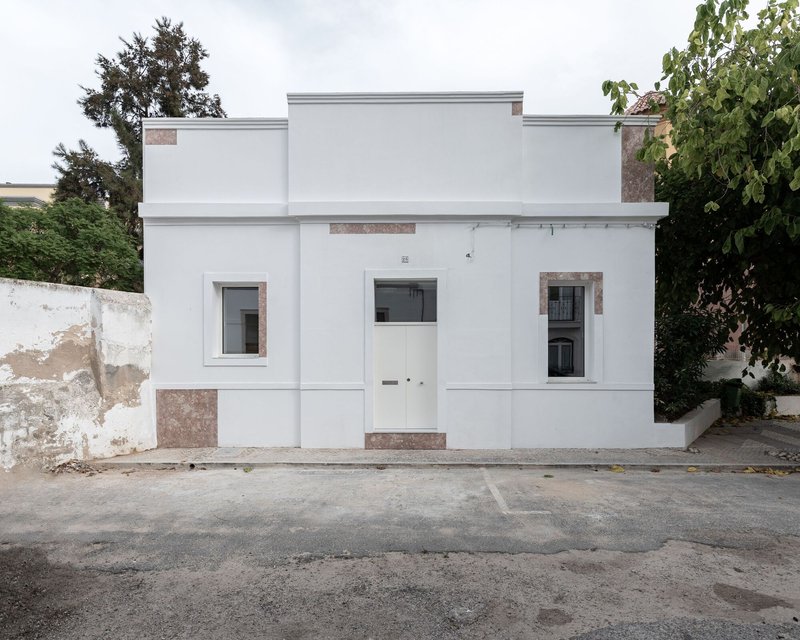 Street facade with white stucco walls and stone accents flanked by weathered perimeter walls and trees