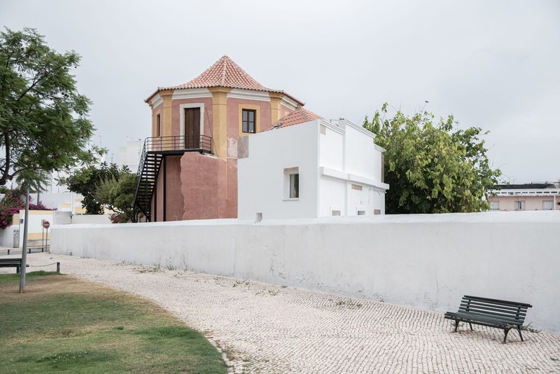Octagonal tower with terracotta roof tiles adjacent to renovated white volumes under overcast skies
