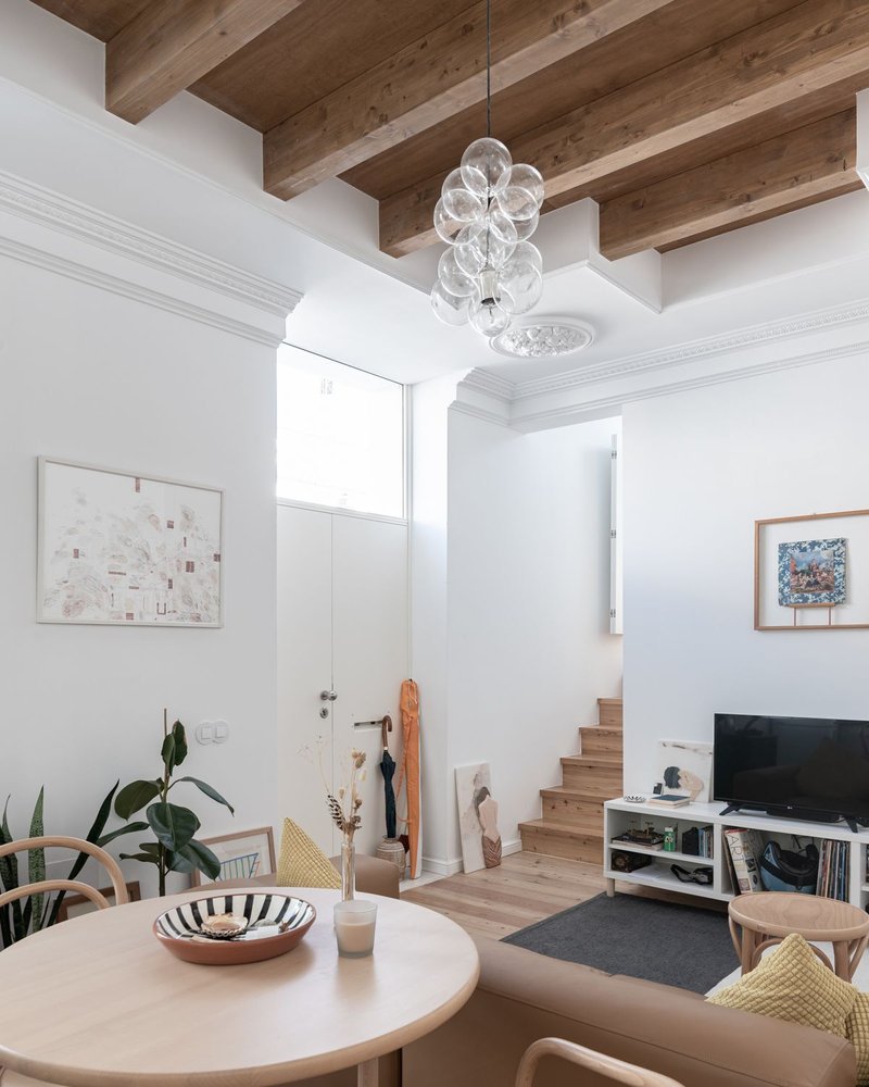 Double-height living space with exposed timber beams and a glass bubble chandelier over a dining table