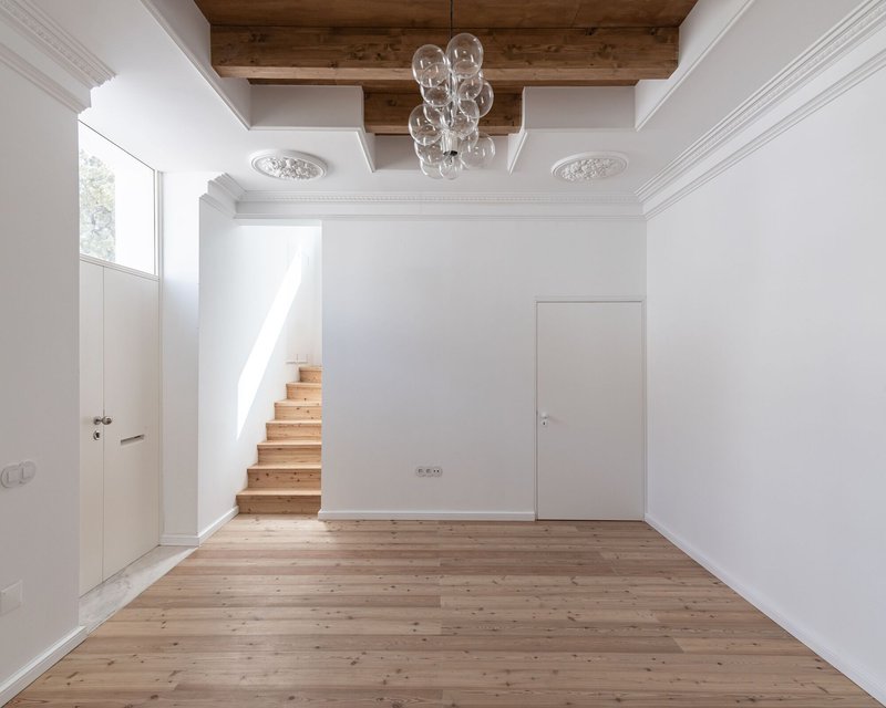 White interior with timber staircase emerging from the wall below exposed timber ceiling beams