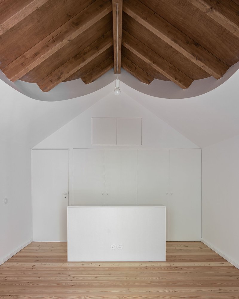 Attic bedroom with curved timber ceiling beams and built-in white storage cabinets below a gable