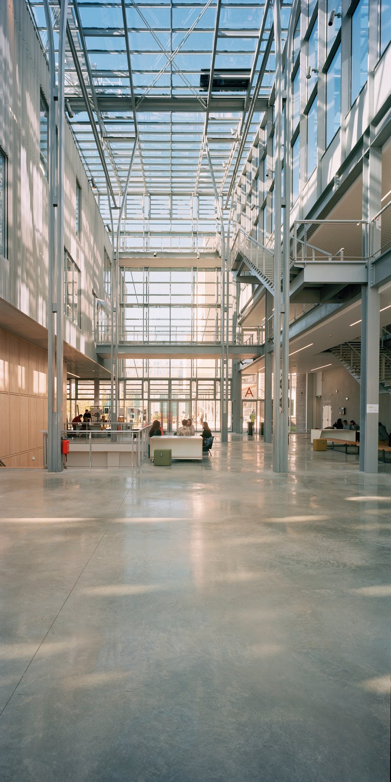 Interior atrium with glass roof structure and steel columns casting shadows on polished concrete floor