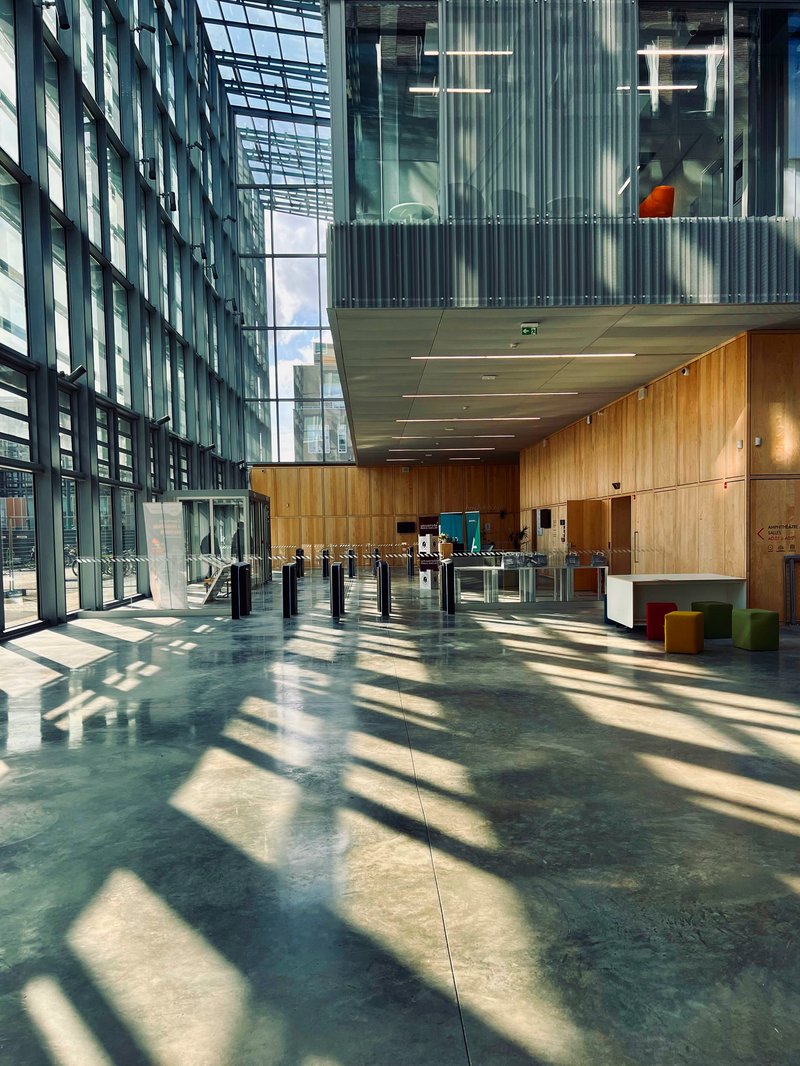 Lobby entrance with timber-clad reception desk and turnstiles beneath translucent ceiling panels filtering daylight