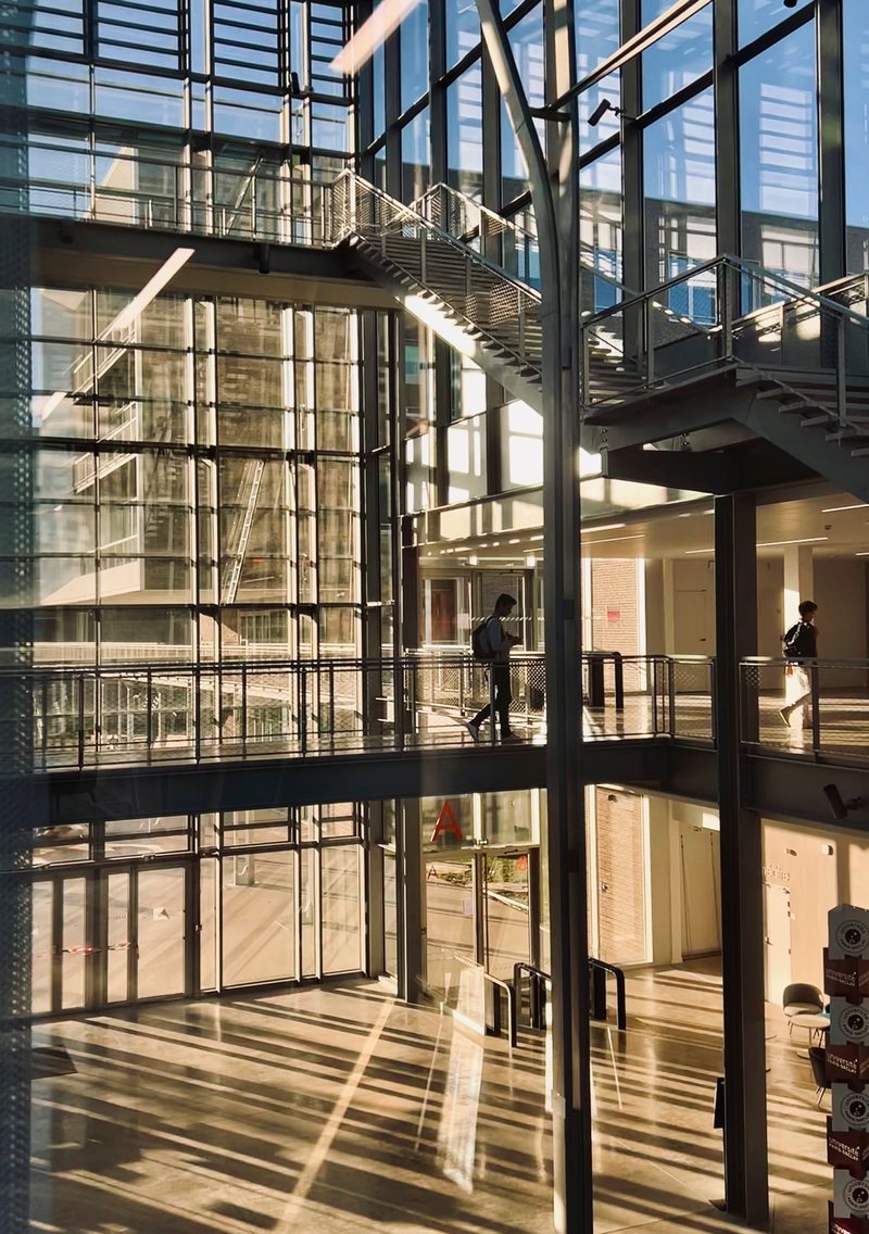 Multi-story atrium with steel bridges spanning between glass-walled floors and exposed structural columns in afternoon light