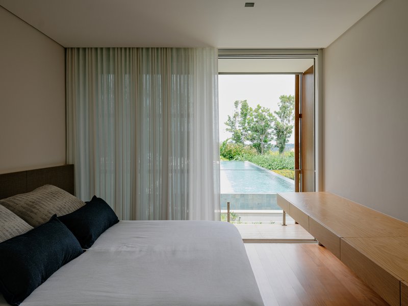 Bedroom with timber desk and open pivot door revealing an infinity pool edge and distant trees