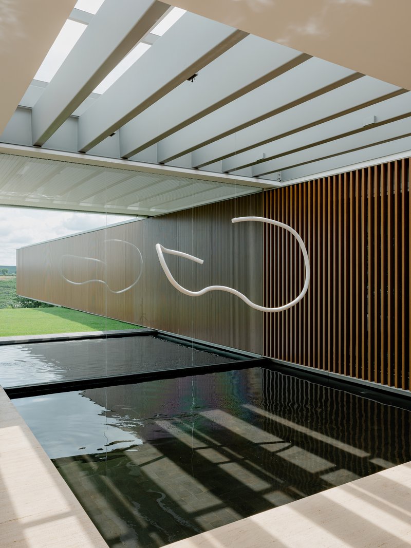 Indoor lap pool with dark tile lining beneath exposed timber beams and skylights running the length