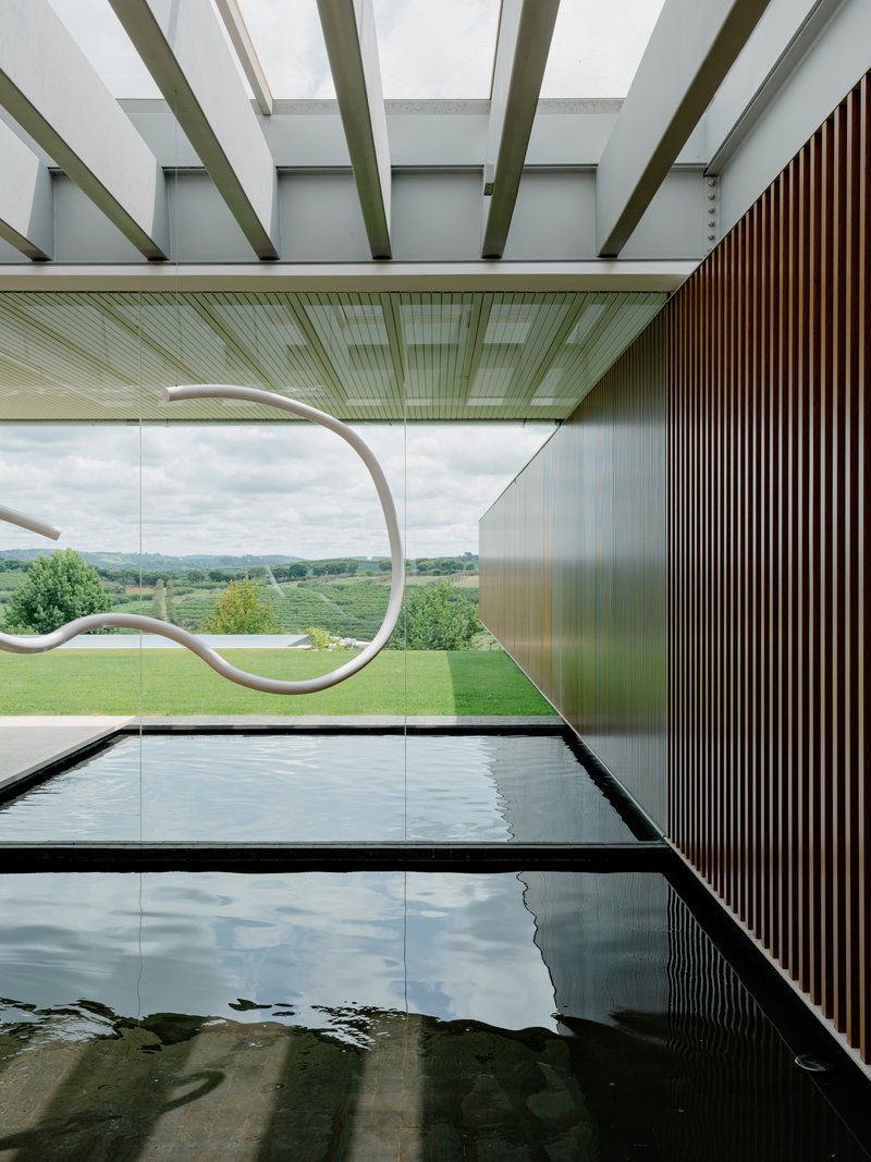 View along the indoor pool showing timber slat wall and full-height glazing overlooking the landscape